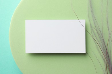 Empty business card, decorative podium and plant on light blue background, top view. Mockup for design