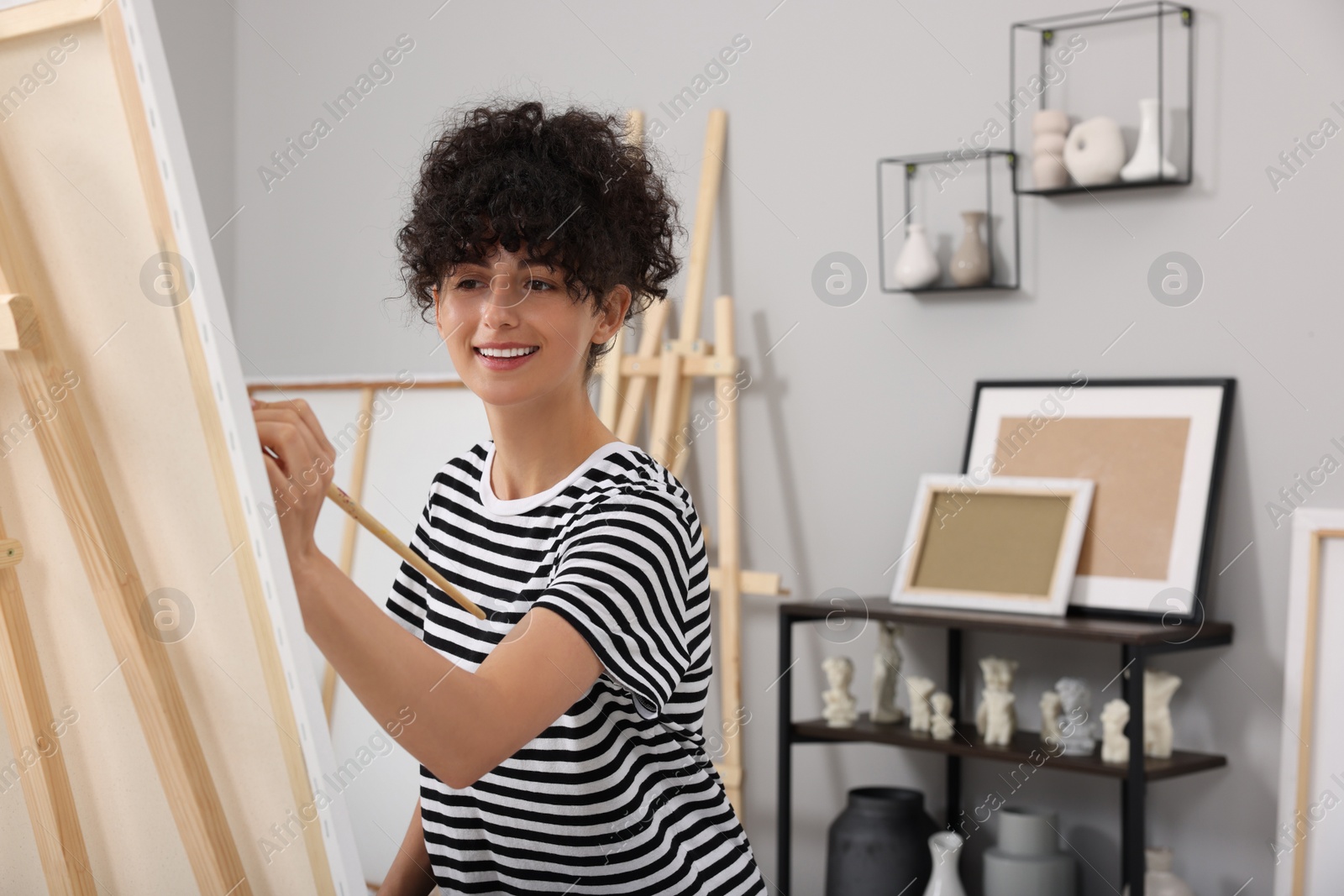 Photo of Young woman painting on easel with canvas in studio