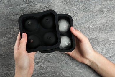 Woman holding mold with frozen ice balls at grey table, top view