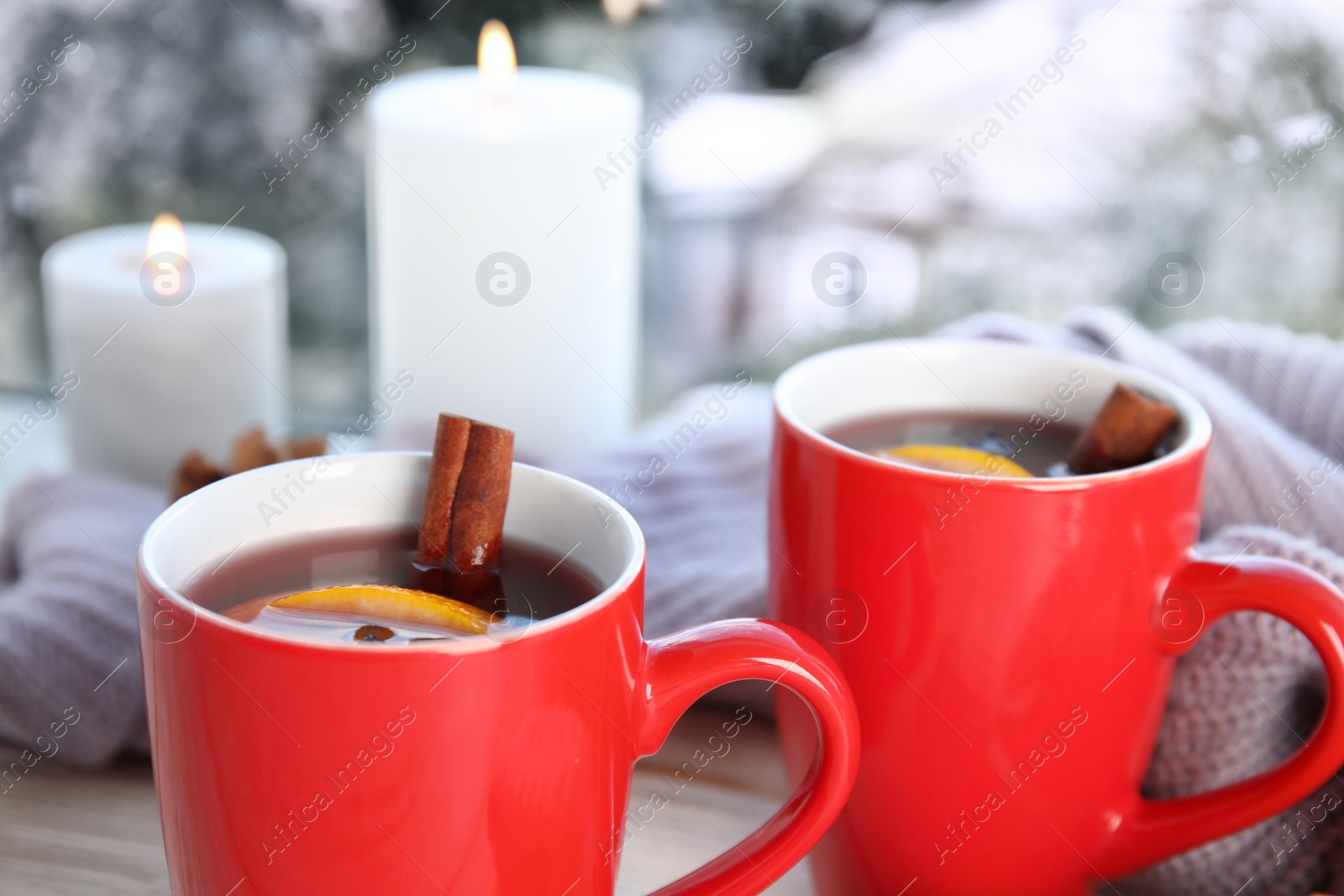 Photo of Cups of hot winter drink with knitted sweater on window sill indoors, closeup