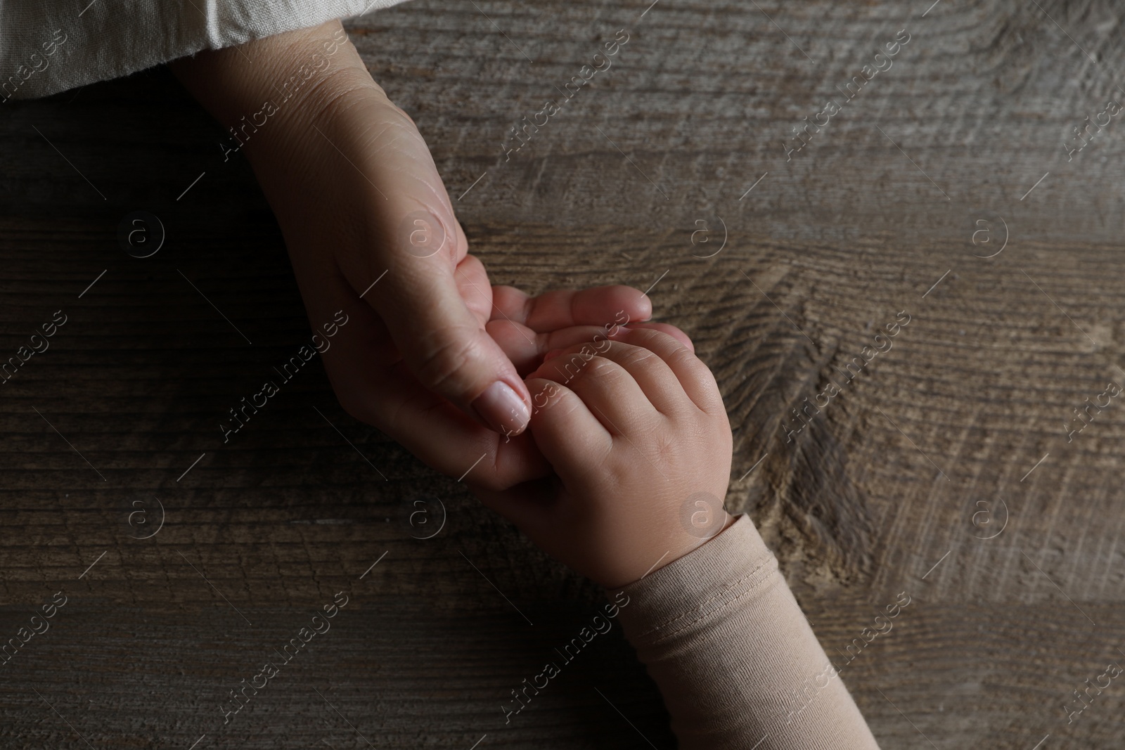 Photo of Woman holding hands with her granddaughter at wooden table, top view. Space for text