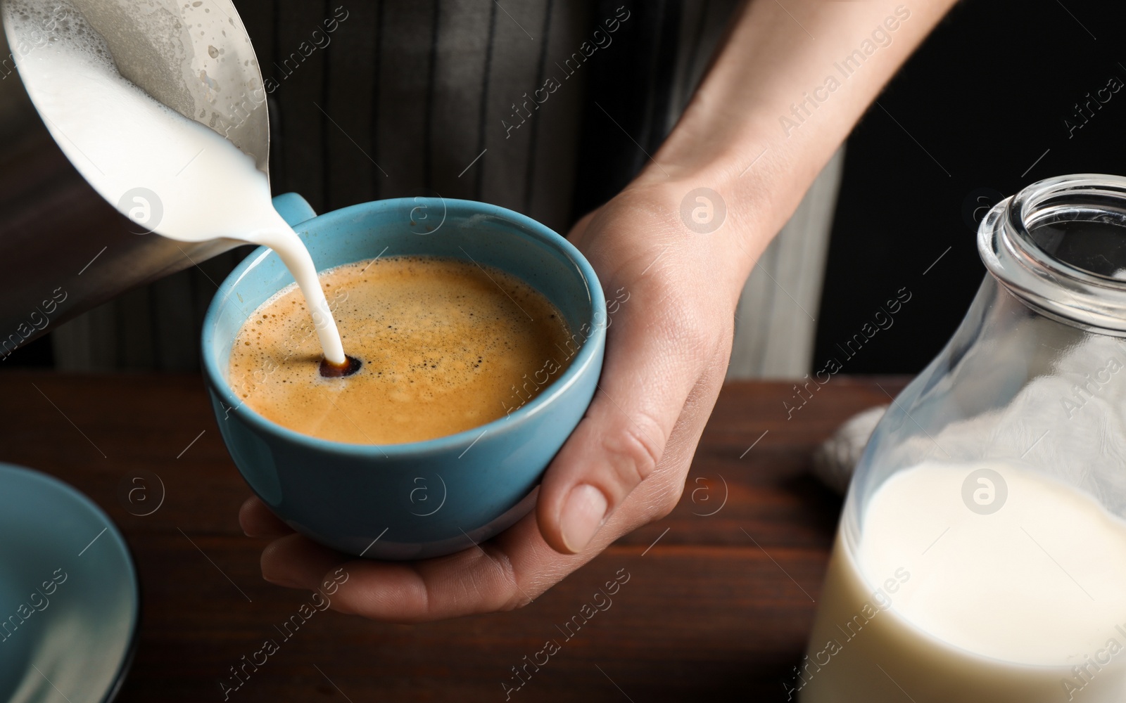 Photo of Woman pouring milk into cup of hot coffee, closeup