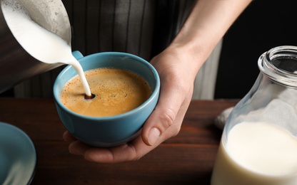 Woman pouring milk into cup of hot coffee, closeup