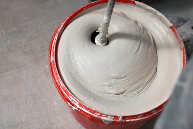 Photo of Mixing putty with electric mixer in red bucket indoors, above view