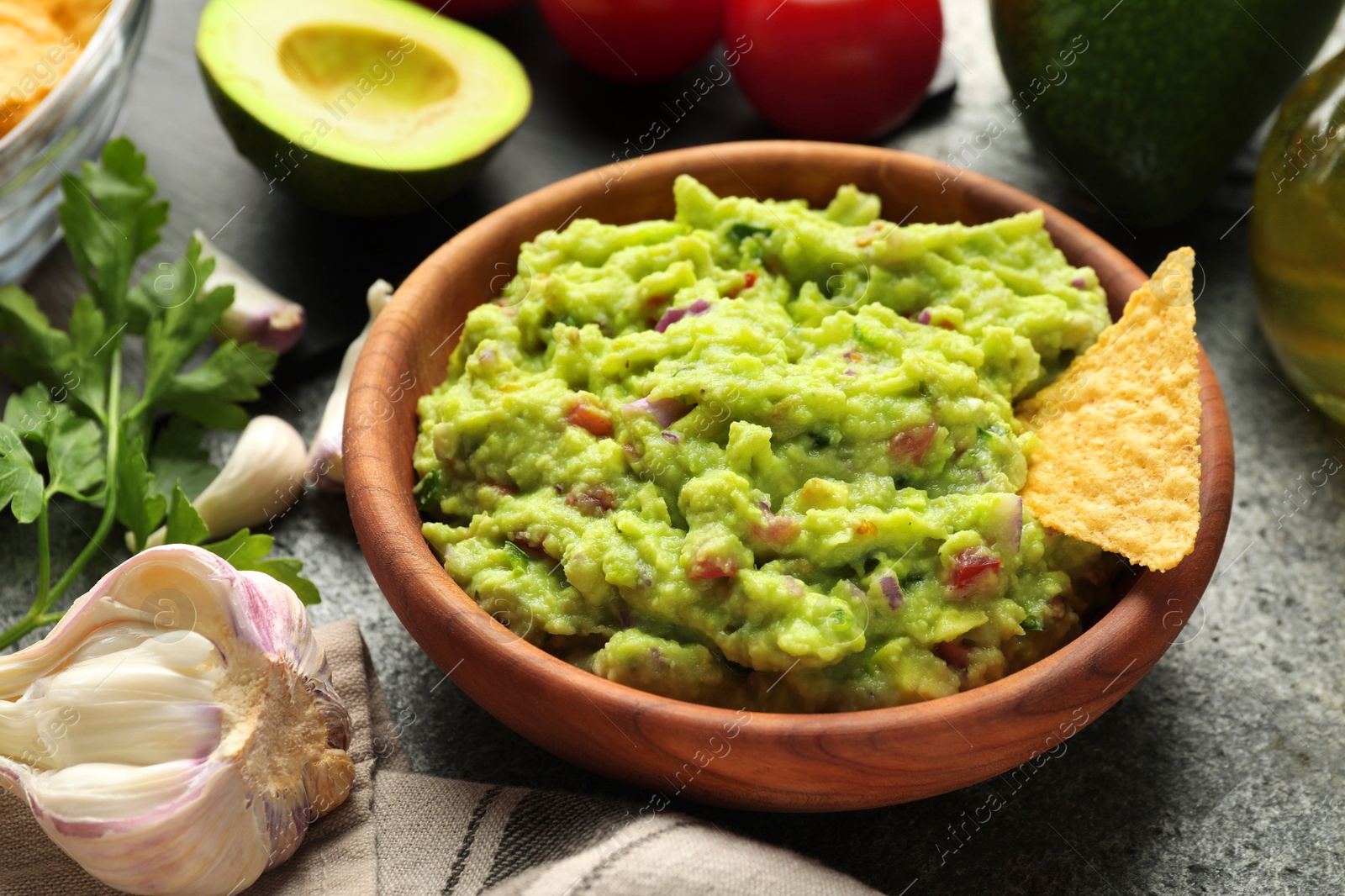 Photo of Delicious guacamole with nachos chips and ingredients on grey table, closeup