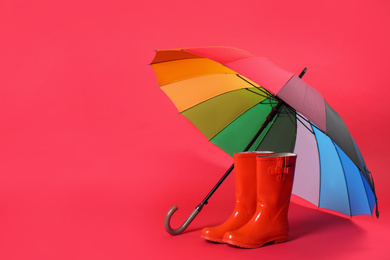 Photo of Colorful umbrella and rubber boots on red background. Space for text