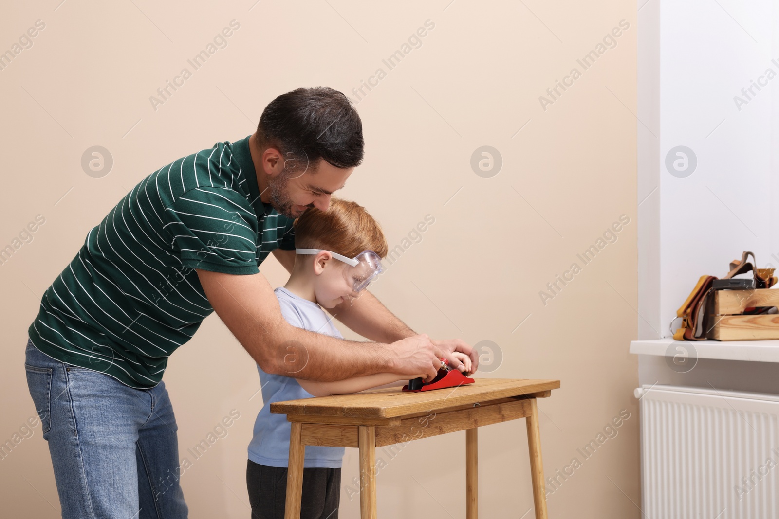 Photo of Father teaching son how to work with plane indoors