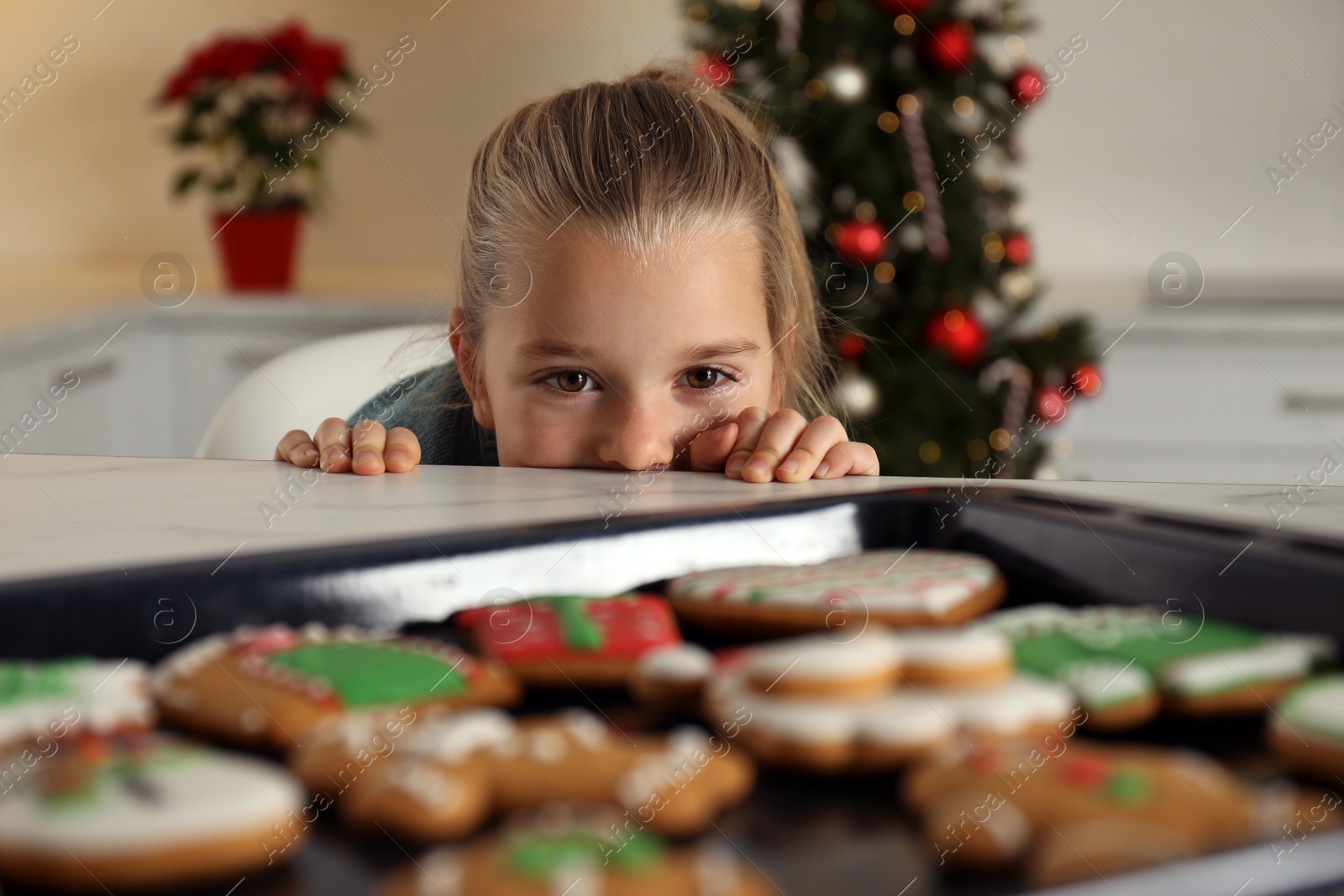 Photo of Cute little girl near baking sheet with fresh Christmas gingerbread cookies indoors