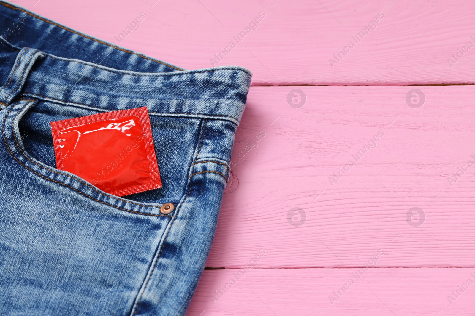 Photo of Packaged condom in jeans pocket on pink wooden table, space for text. Safe sex