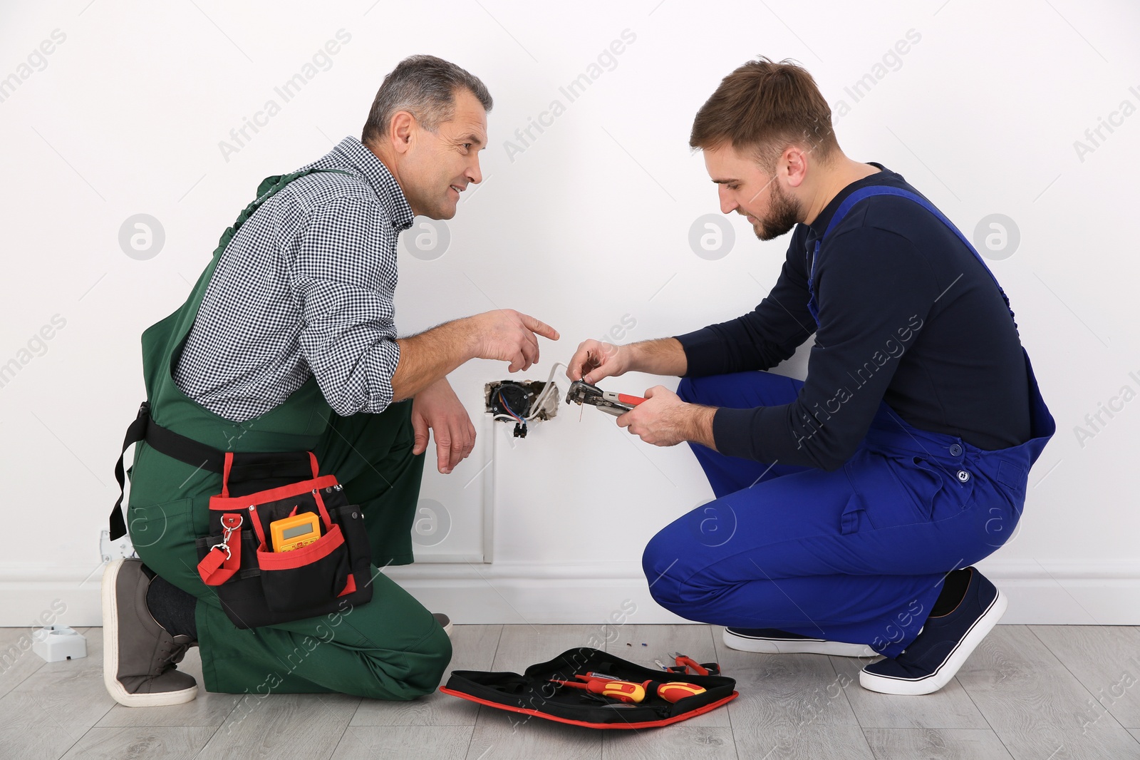 Photo of Senior electrician helping trainee stripping wire ends indoors