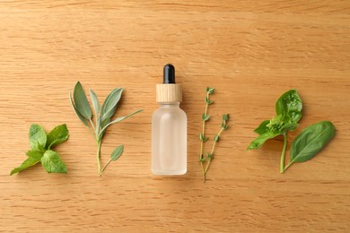 Photo of Bottle of essential oil and fresh herbs on wooden table, flat lay