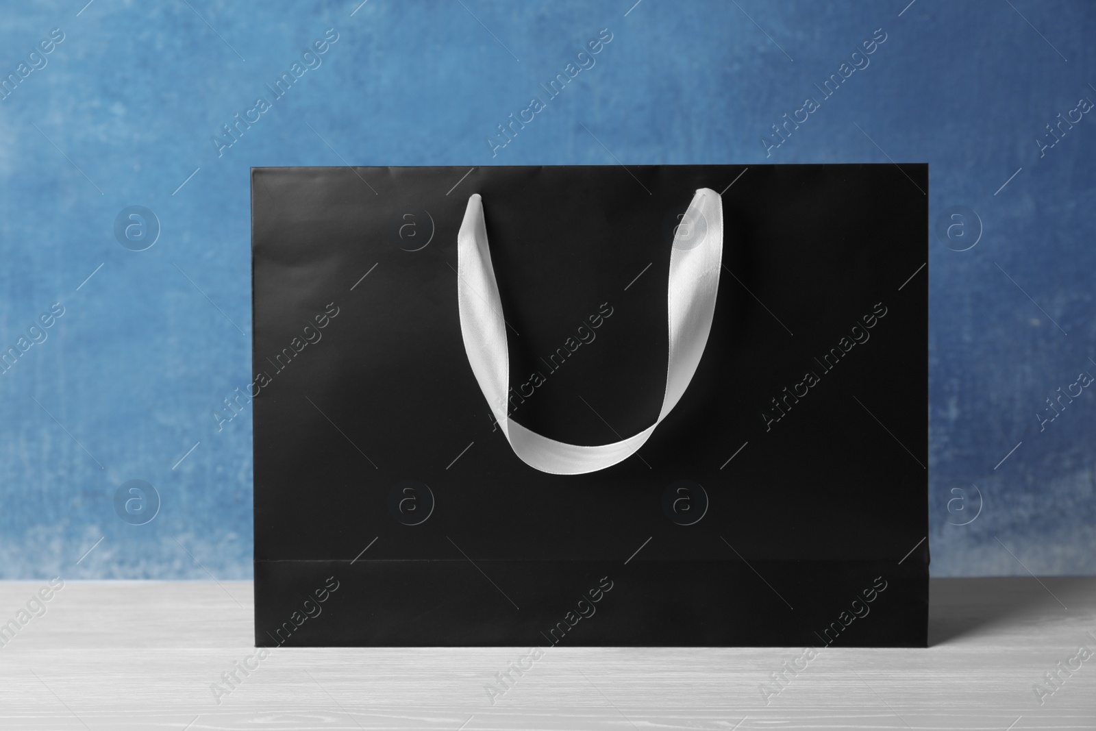 Photo of Paper shopping bag with handles on table against color wall. Mock up for design