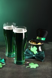 Photo of St. Patrick's day celebration. Green beer, leprechaun hat, pot of gold and decorative clover leaves on grey table. Space for text
