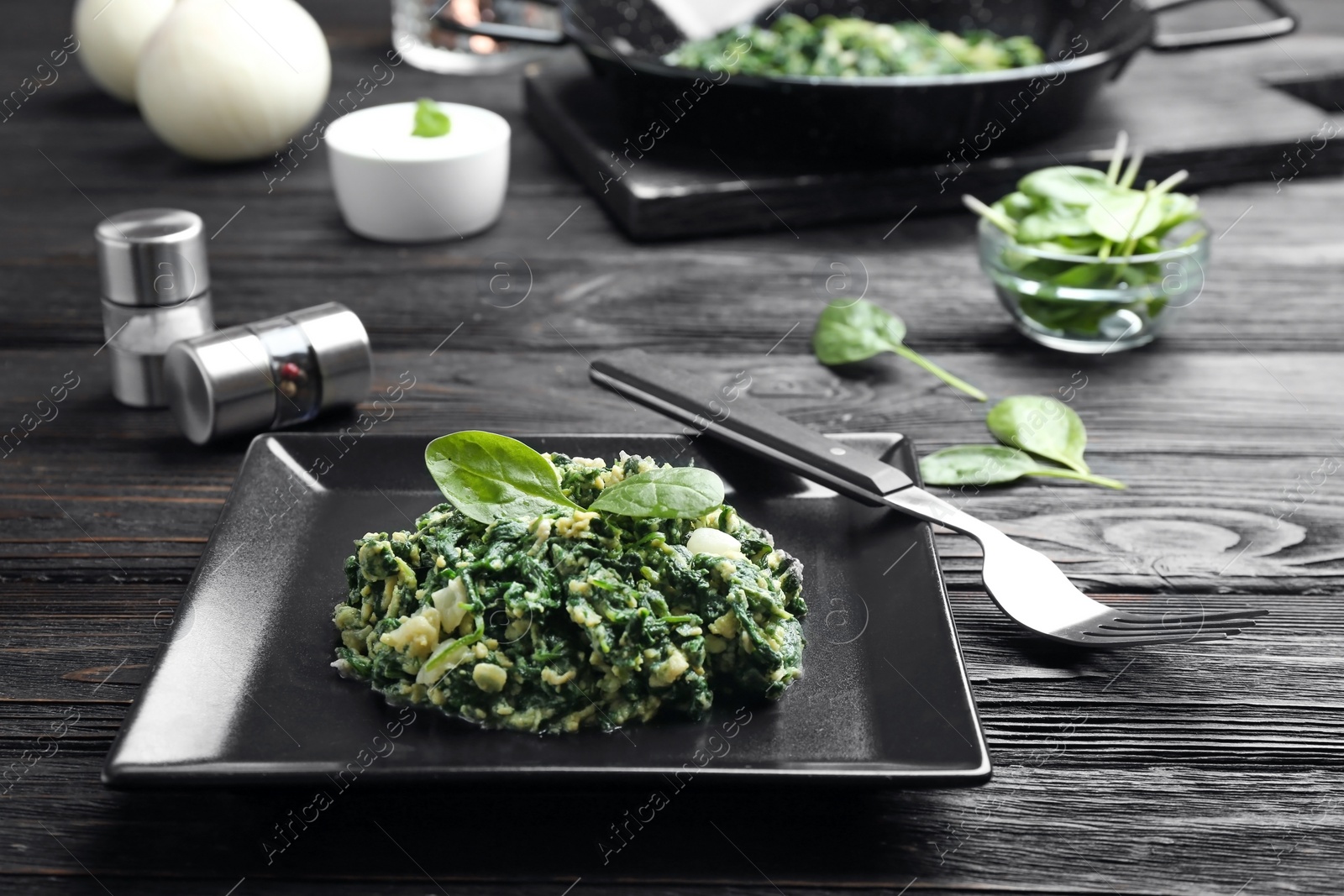 Photo of Tasty spinach served on black wooden table. Healthy food