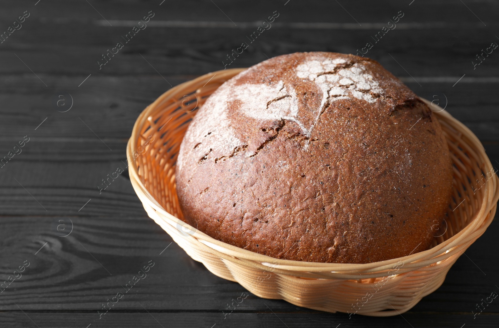 Photo of Wicker basket with fresh bread on black wooden table