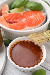 Photo of Fresh marinade, fish and brush on white wooden table, closeup