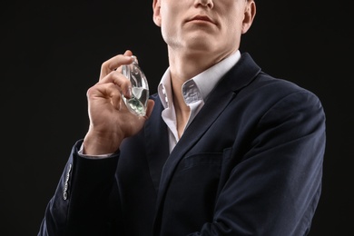 Photo of Handsome man in suit using perfume on black background, closeup