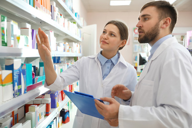 Professional pharmacists near shelves in modern drugstore