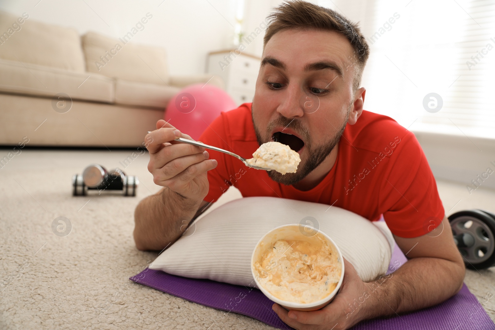 Photo of Lazy young man eating ice cream instead of training at home