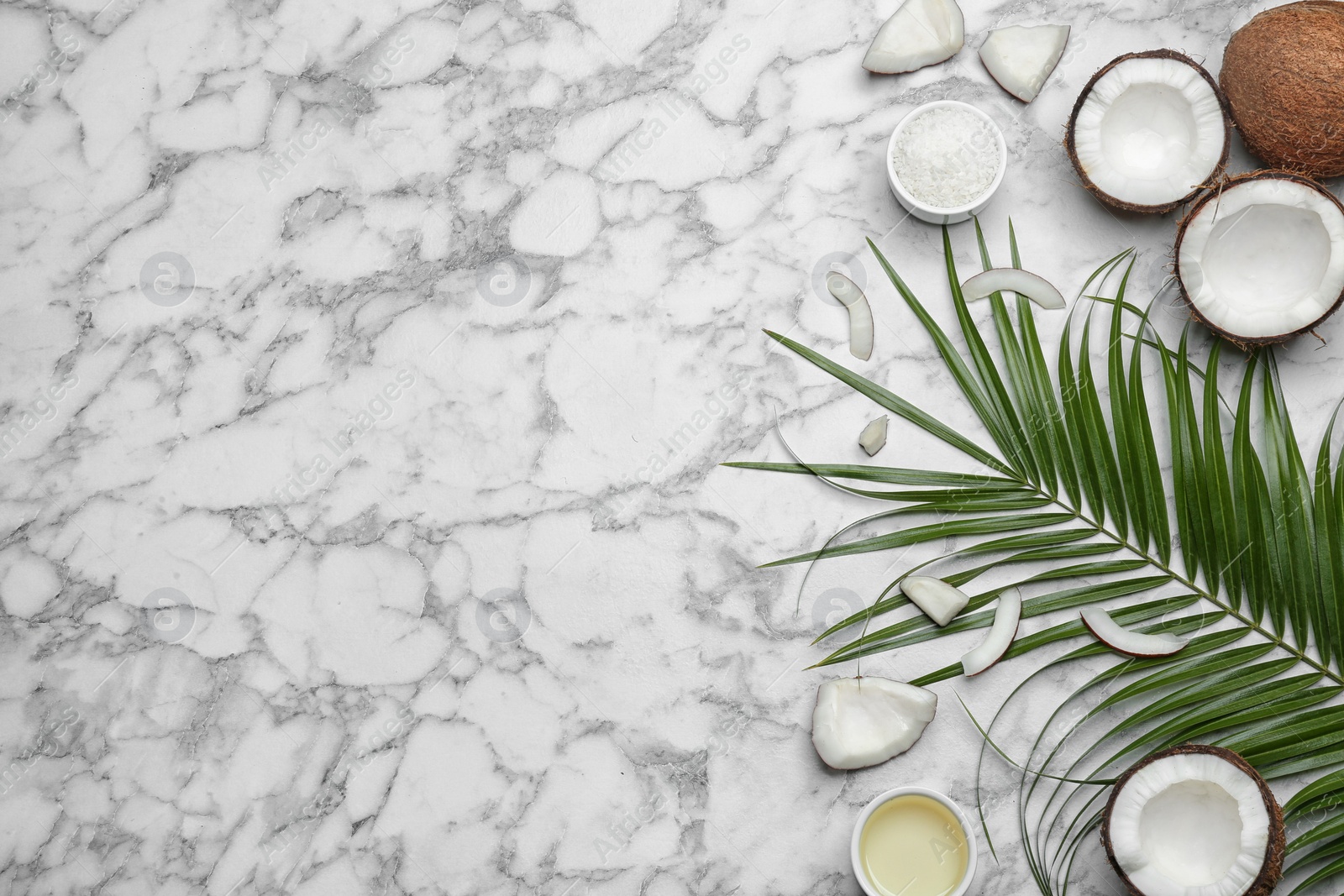 Photo of Bowl of natural organic oil and coconuts on marble background, flat lay. Space for text