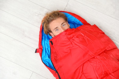 Young man in comfortable sleeping bag on floor, top view