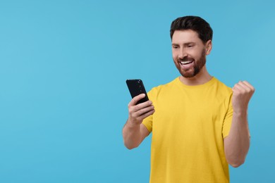 Happy man using smartphone on light blue background. Space for text