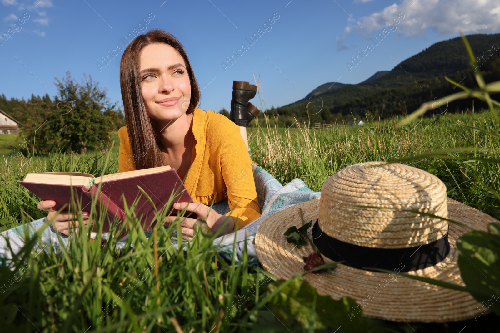 Photo of Beautiful young woman reading book on green meadow in mountains