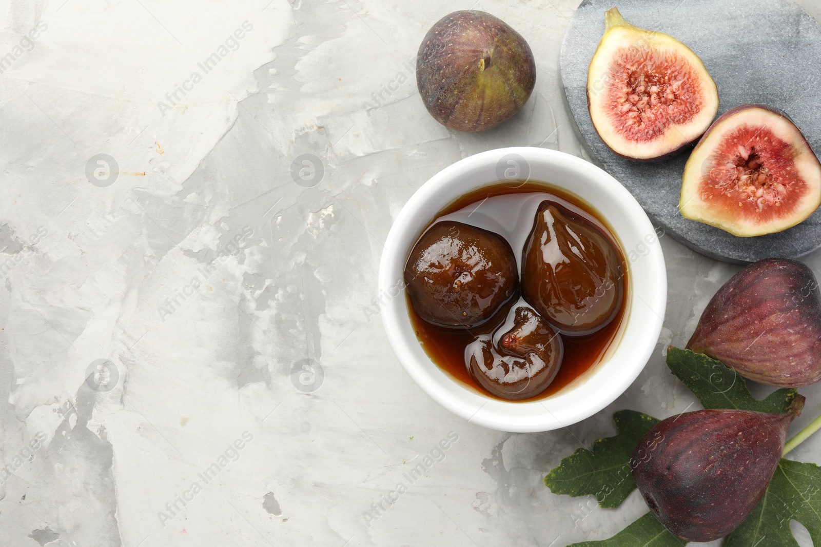 Photo of Bowl of tasty sweet jam and fresh figs on grey table, flat lay. Space for text