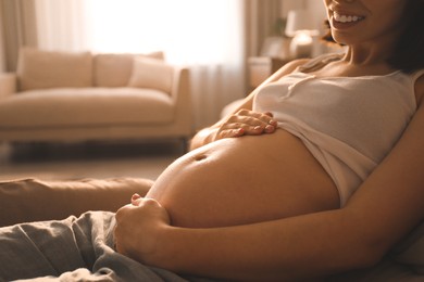 Photo of Pregnant young woman touching belly at home, closeup