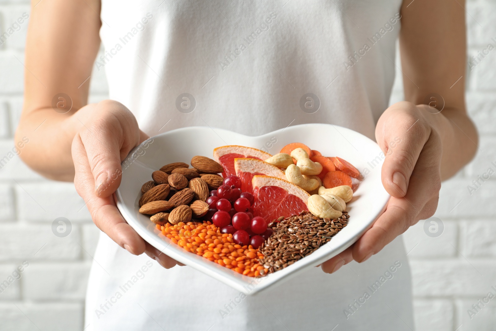 Photo of Woman holding plate with products for heart-healthy diet, closeup