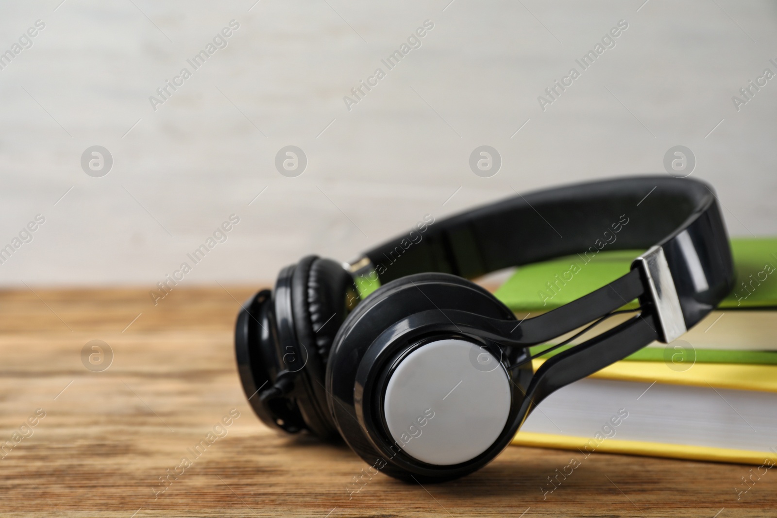 Photo of Modern headphones with hardcover books on wooden table, closeup. Space for text