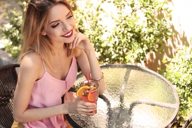 Young woman with glass of tasty lemonade at table in cafe, outdoors. Natural detox drink