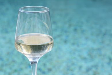 Glass of tasty wine near swimming pool, closeup. Space for text