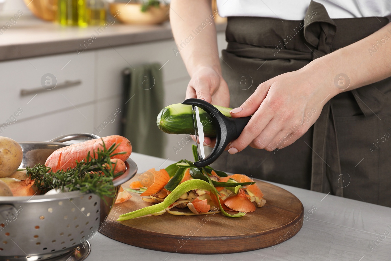 Photo of Woman peeling fresh cucumber at light table indoors, closeup