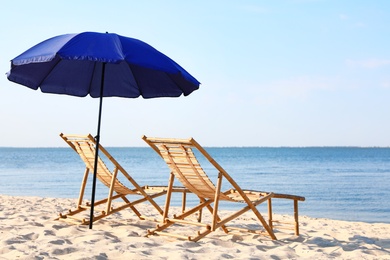 Photo of Empty wooden sunbeds and umbrella on sandy shore. Beach accessories