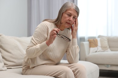 Overwhelmed woman with glasses sitting on sofa at home