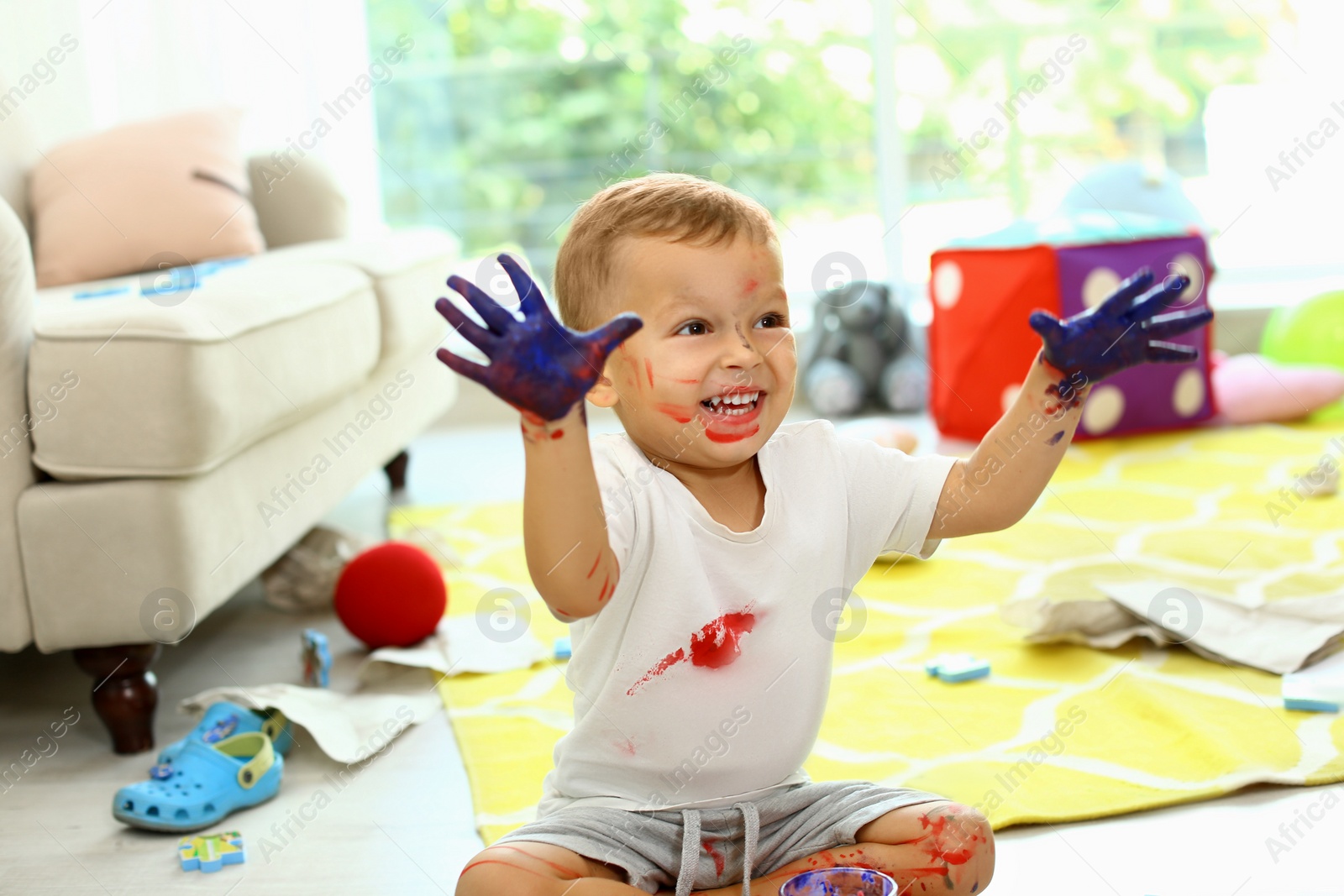 Photo of Cute little boy playing with paints on floor in living room