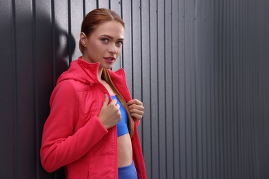 Beautiful woman in gym clothes posing near dark grey wall on street, space for text