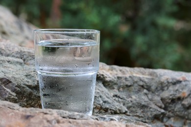 Photo of Glass of water on stone outdoors, closeup. Space for text