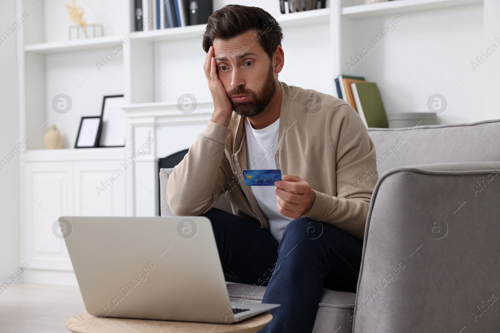 Photo of Upset man with credit card near laptop at home. Be careful - fraud