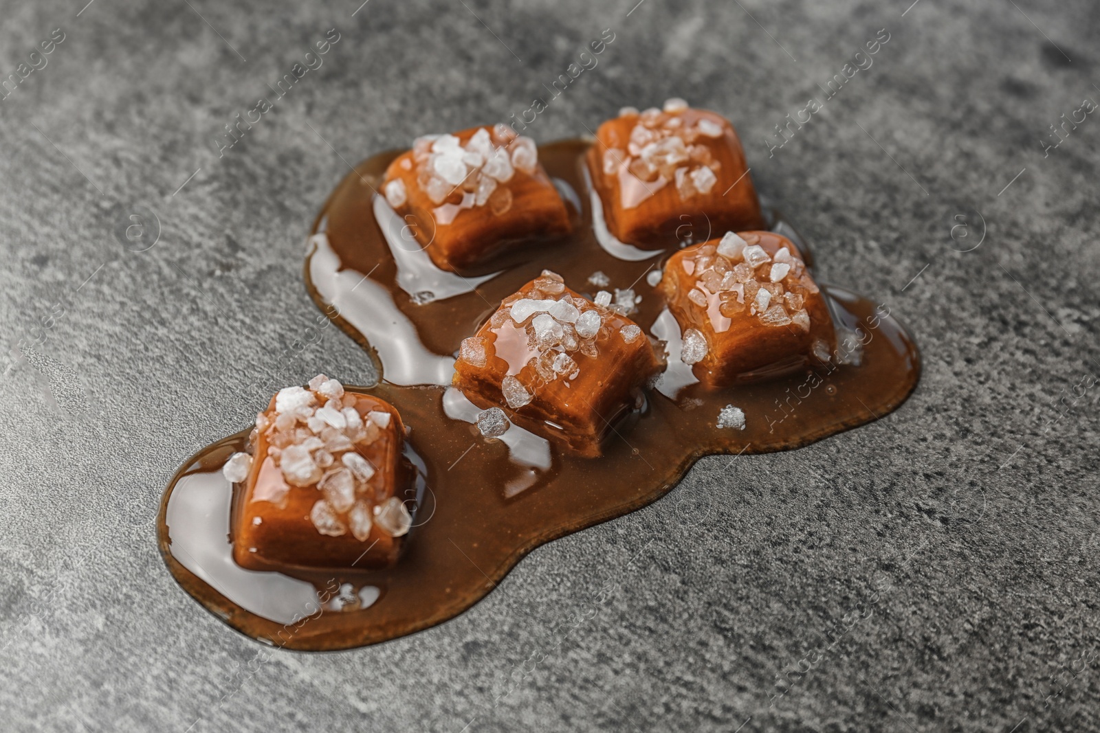 Photo of Delicious candies with caramel sauce and salt on gray background