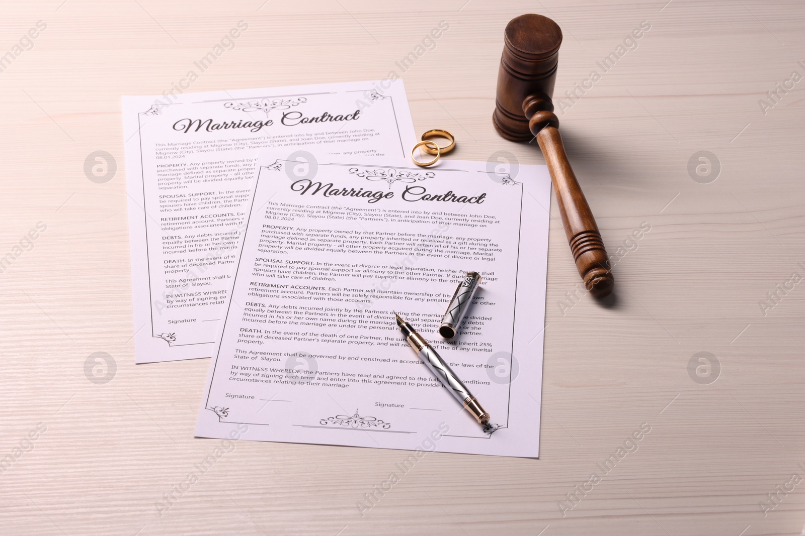 Photo of Marriage contracts, gold rings, gavel and pen on light wooden table, above view