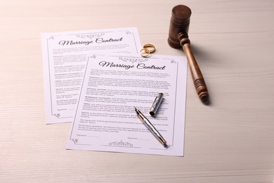 Marriage contracts, gold rings, gavel and pen on light wooden table, above view