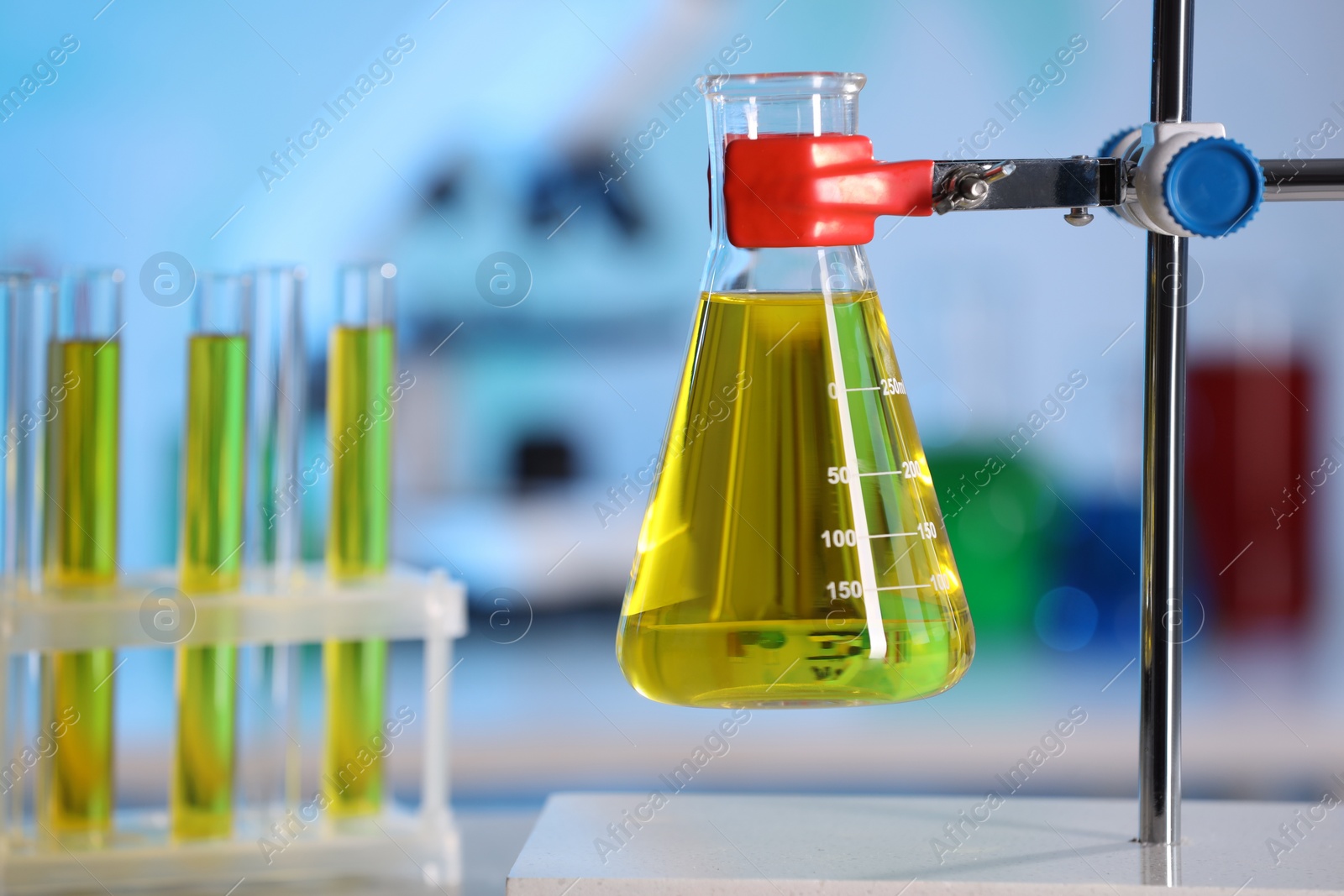 Photo of Flask with yellow liquid on retort stand in laboratory, closeup. Space for text