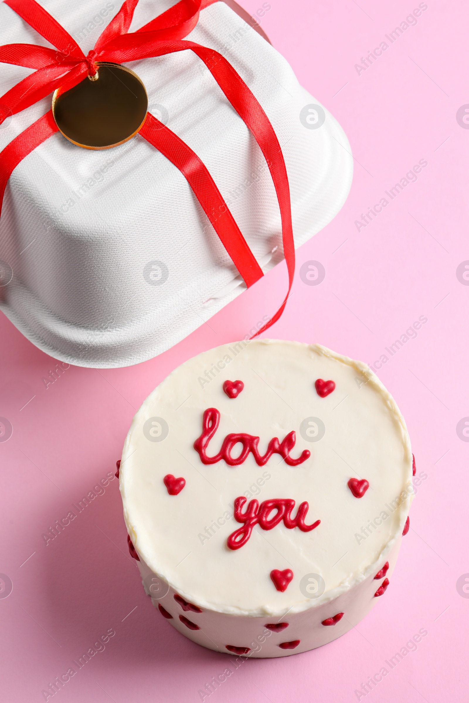 Photo of Bento cake with text Love You and takeaway packaging on pink table, above view. St. Valentine's day surprise