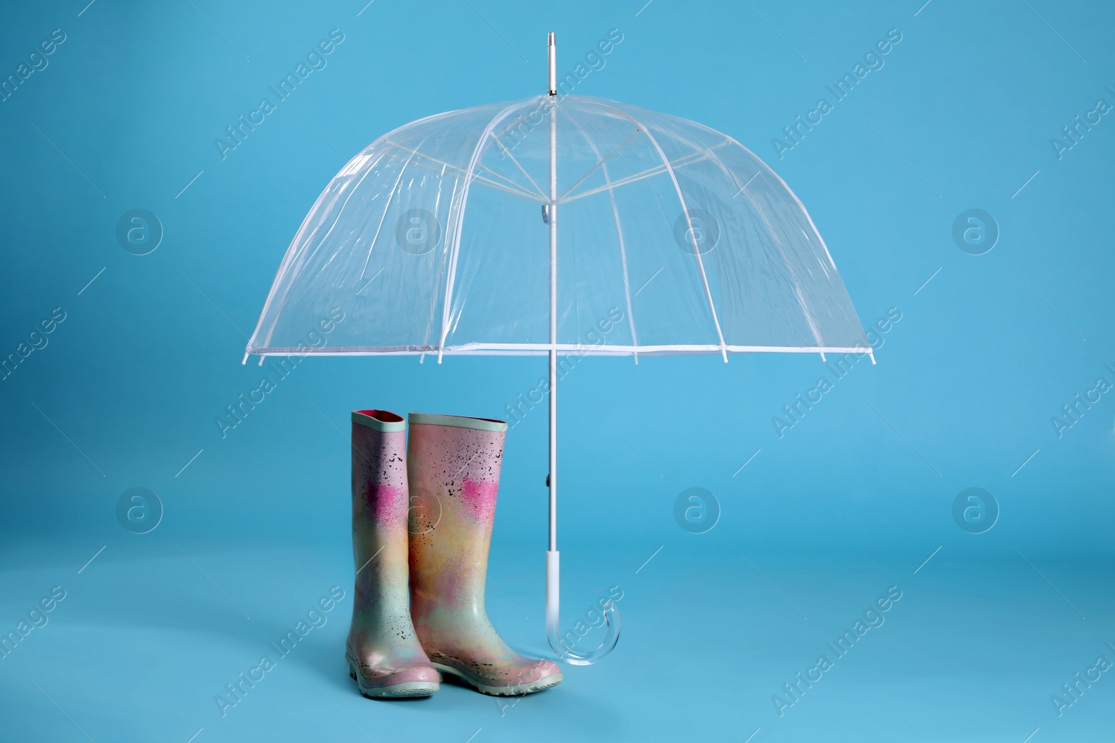 Photo of Open transparent umbrella and rubber boots on light blue background