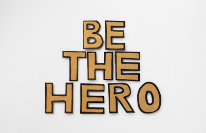 Photo of Phrase Be The Hero made of cardboard letters on white background, flat lay