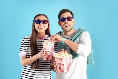 Couple with 3D glasses and tasty popcorn on color background