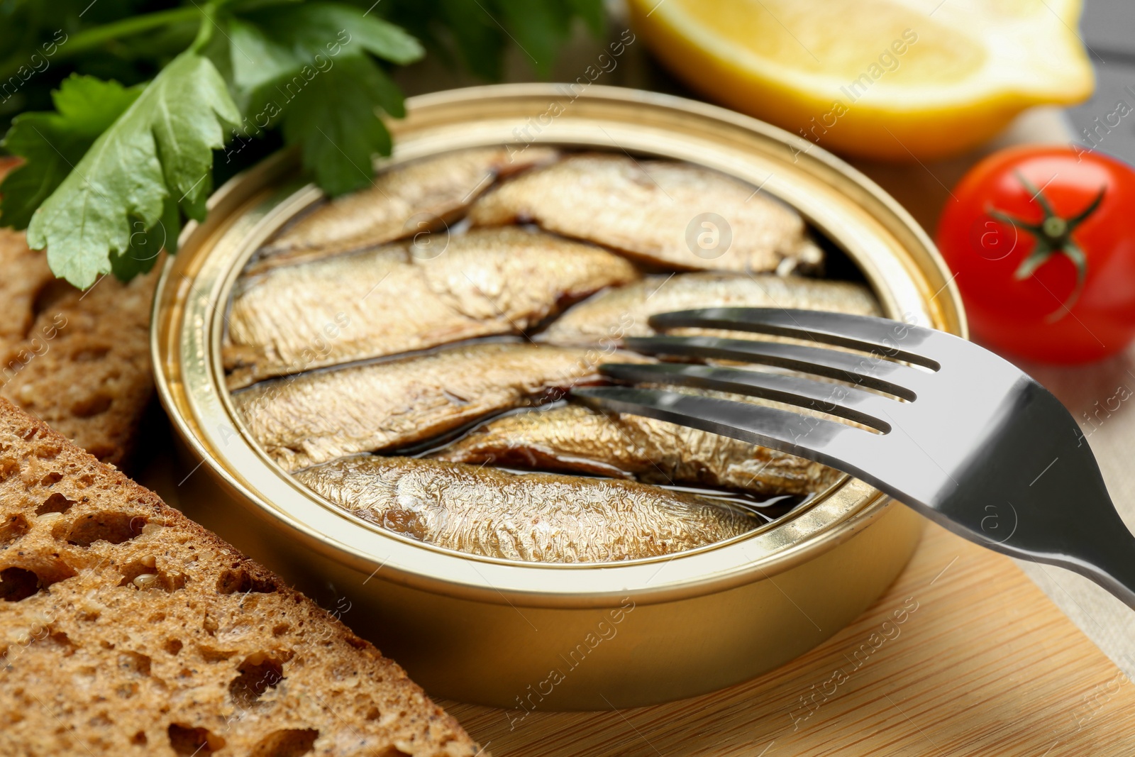 Photo of Tin can with tasty sprats served on wooden board, closeup