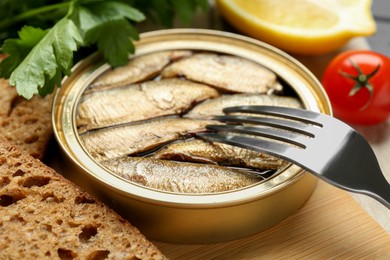 Tin can with tasty sprats served on wooden board, closeup